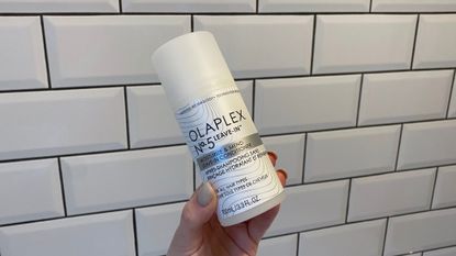 Image showing hand holding the Olaplex No.5 Leave-In Conditioner against a white tiled background