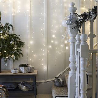 White staircase next to white wall decorated with strings of fairy lights and surrounded by gifts and decorations