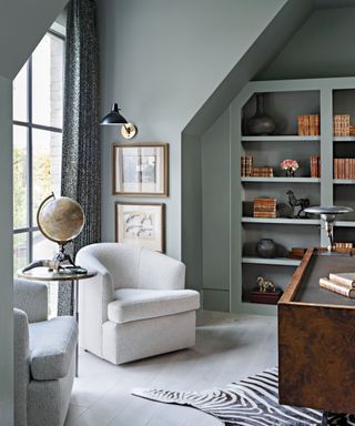 calming home office with blue-gray walls, built-in shelving and white armchairs