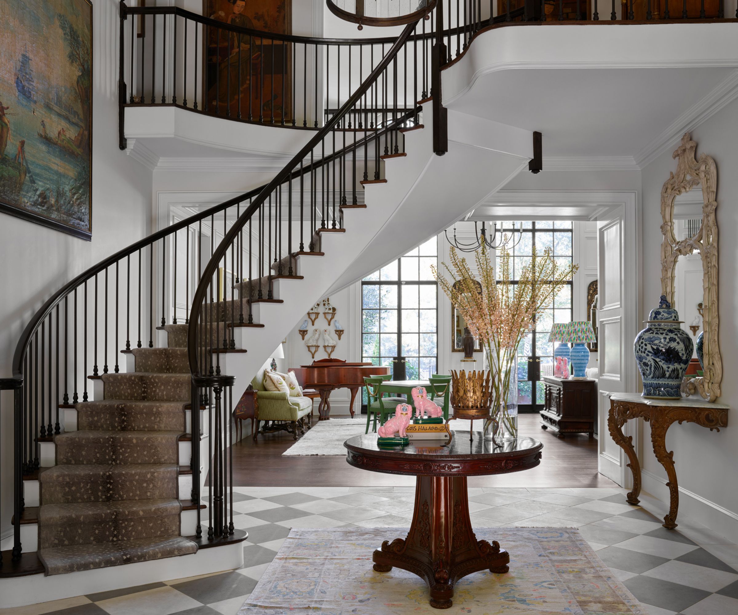 Hallway with spiral staircase, checkerboard tiled floor, mahogany round table, vintage vase and large mirror