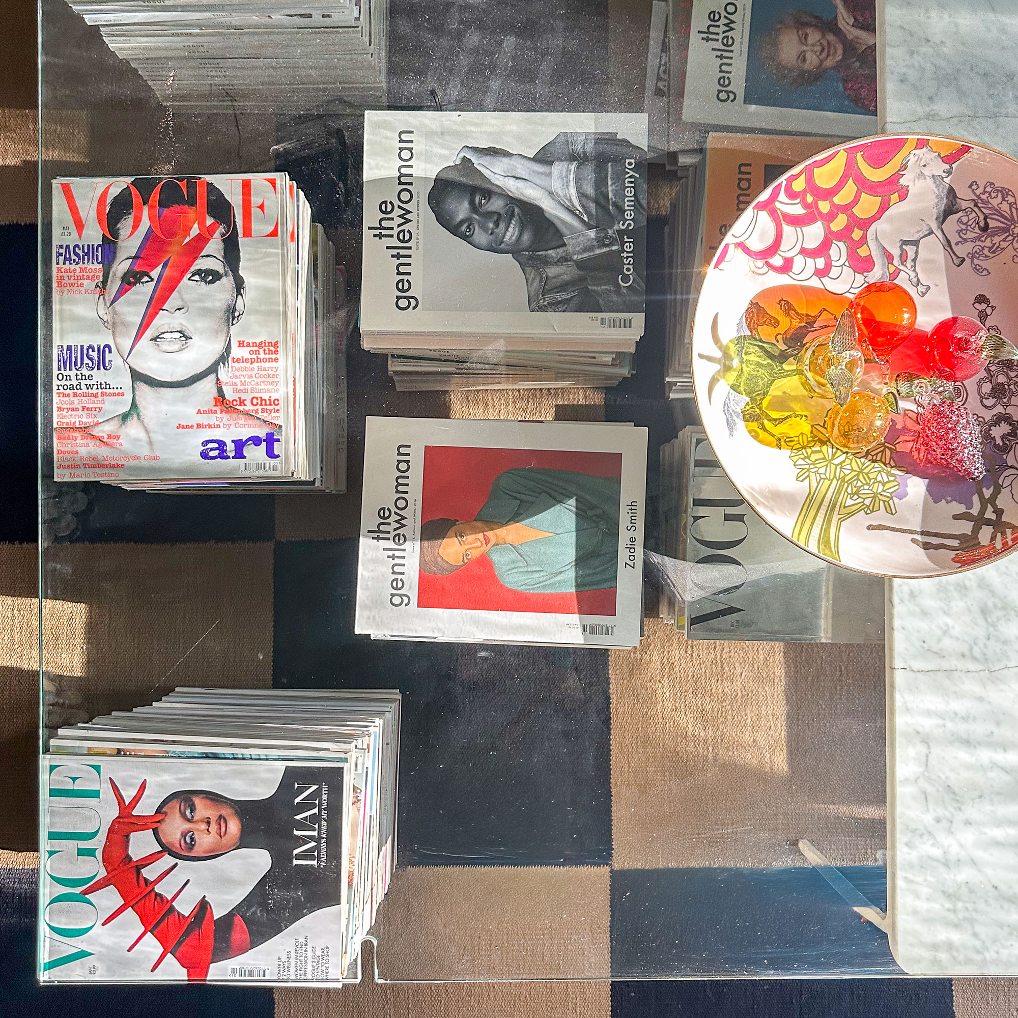 Glass topped coffee table propped up with marble and stacks of magazines