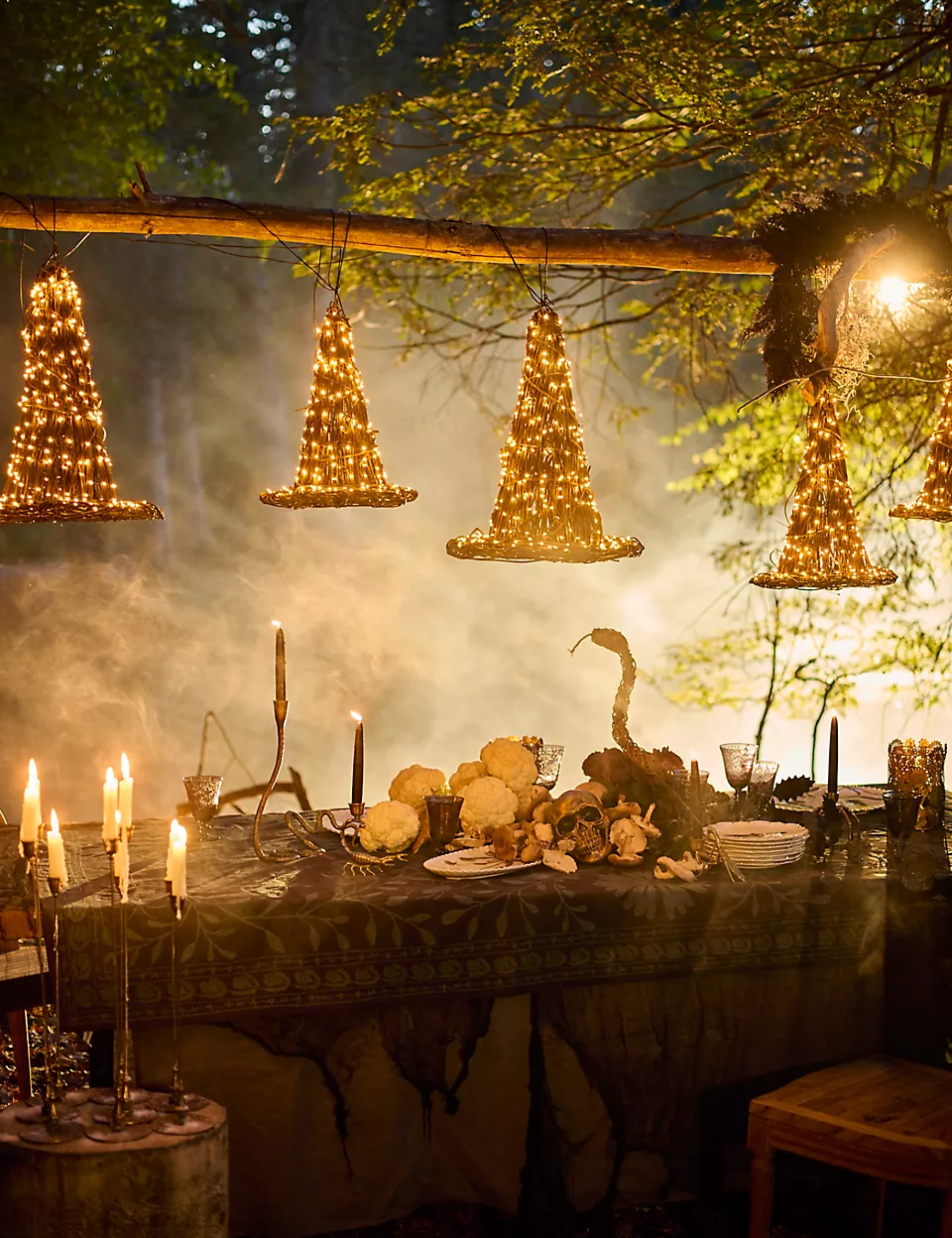 Illuminated LED rattan witch hats hanging overhead a spooky outdoor Halloween dinner party.