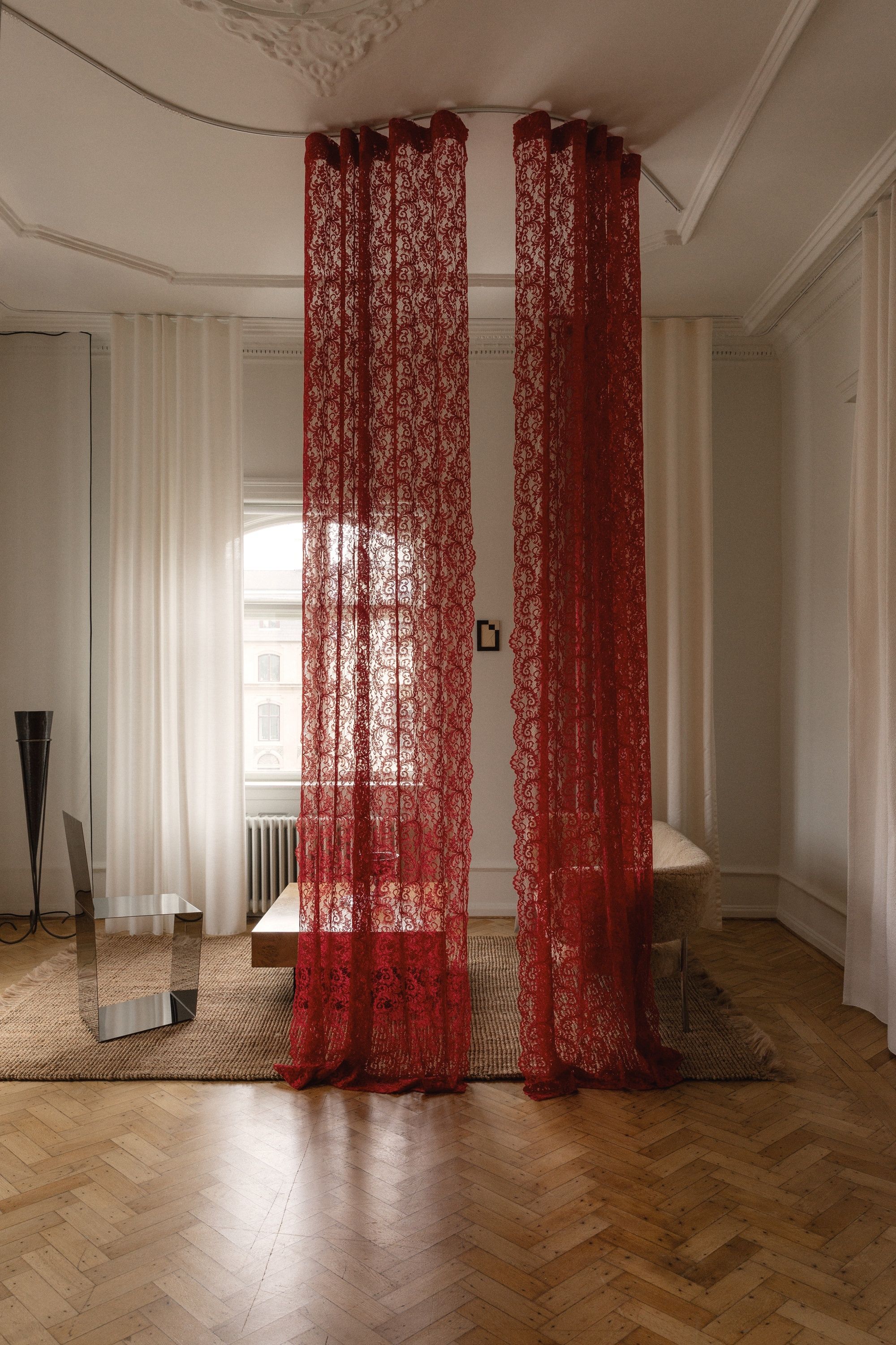red lace curtains hanging in the middle of a room in a heritage building in Copenhagen with parquetry floors and sheers on the windows