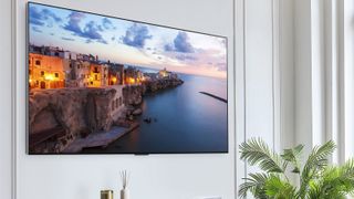 The LG G3 OLED TV mounted on a white wall displaying a scene of a coastal town at night.