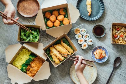  Two people’s hands using chopsticks while sharing Asian food takeout.