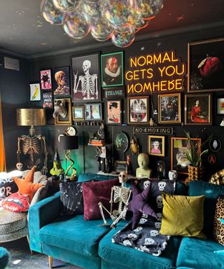 A living room with black walls, wall art prints, neon signs, a bubble chandelier, and a velvet blue couch