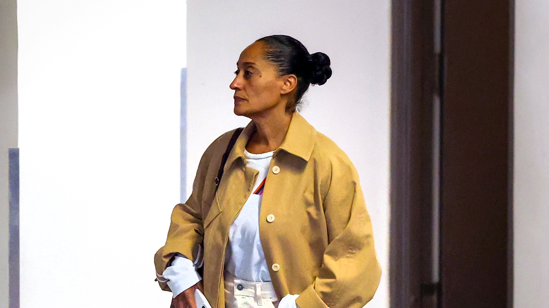 Tracee Ellis Ross wearing a tan trench coat, white tee, white jeans, and white glove flats