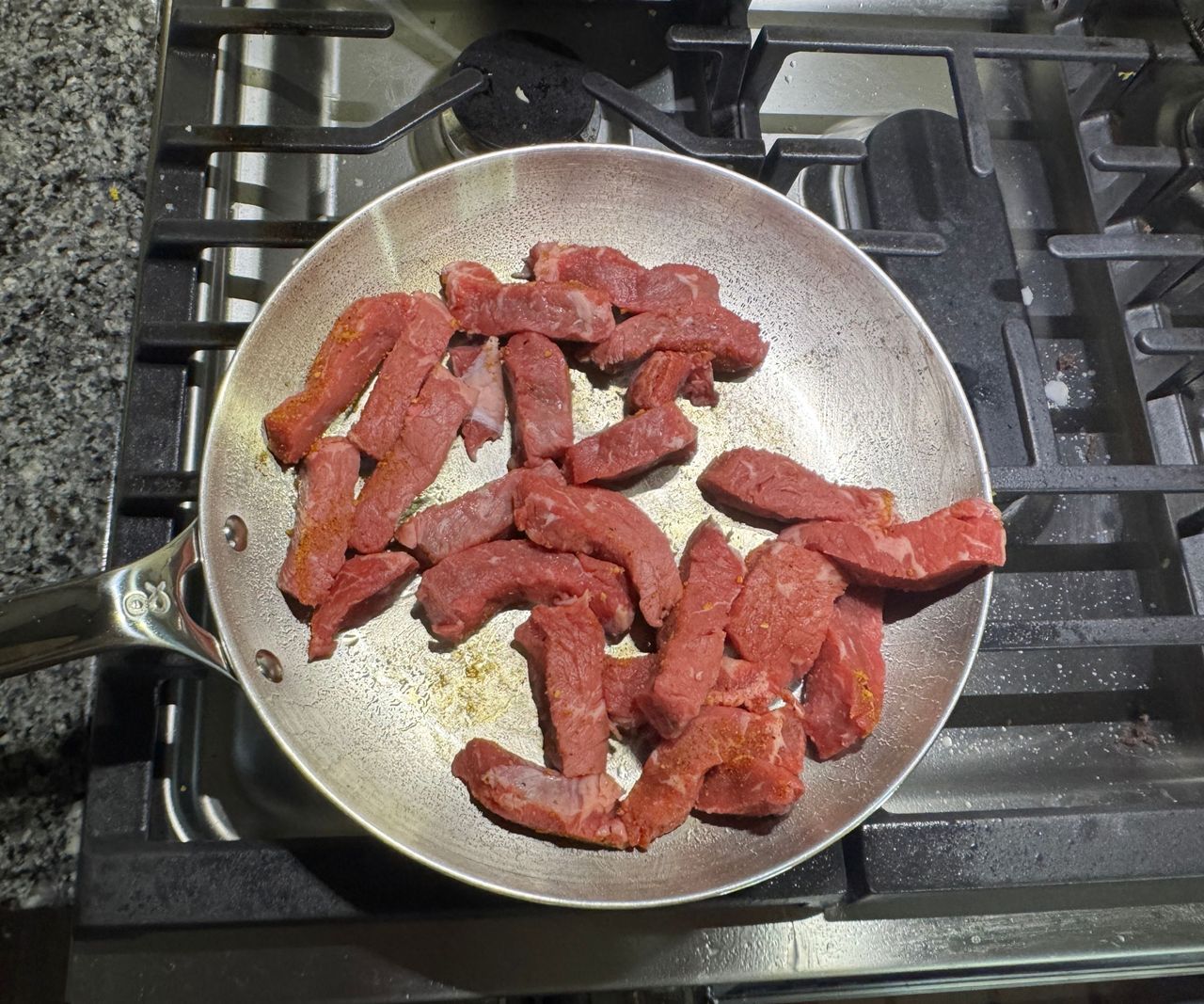 A small stainless steel frying pan on a gas stove filled with raw steak strips