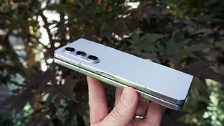 Samsung Galaxy Z Fold 5 holdes opp av en hånd foran grønne busker.