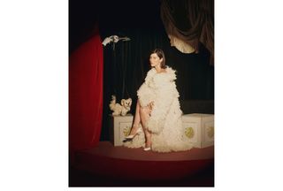 Gracie Abrams wearing a cream-colored furry Stella McCartney long coat with matching Ferragamo heels sitting on a painted chest next to a dog puppet forBest Knockoff Luxury Clothing
's fall issue.