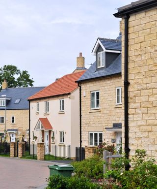 New housing estate of traditional-style developer homes, clad in a mix of render and stone, with black GRP rainwater goods from Yeoman Rainguard in the foreground