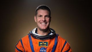 an astronaut smiles for a portrait in an orange spacesuit