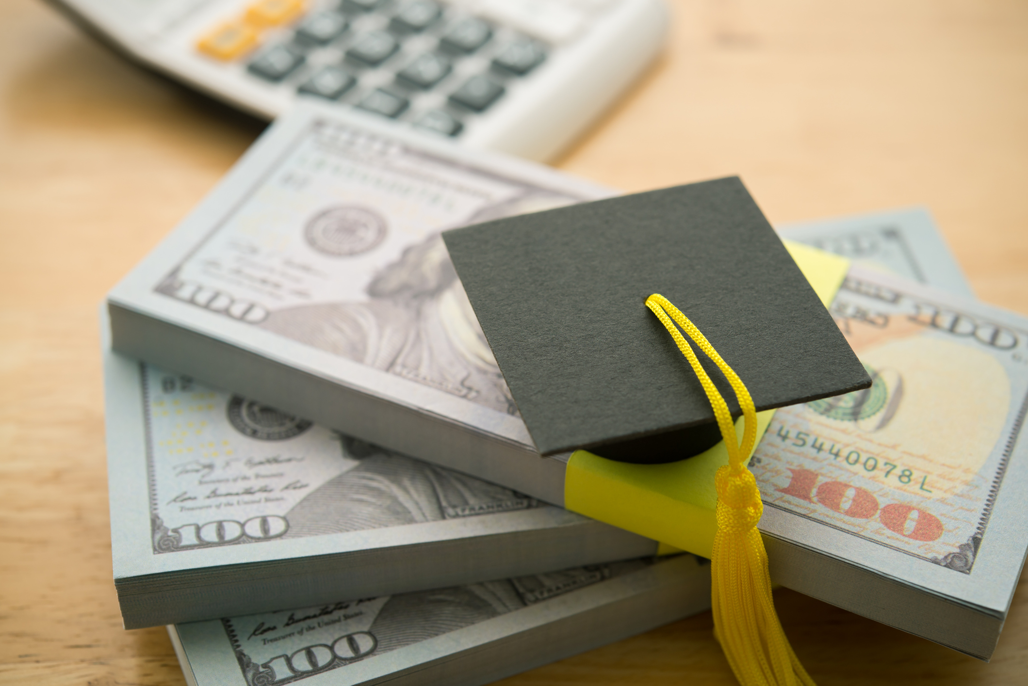 Graduation cap, university or college degree on a stack of US dollar banknotes