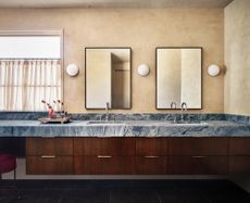 modern bathroom with plaster walls, marble vanity and timber cabinetry, two mirrors with wall sconces, and a window with linen cafe curtains