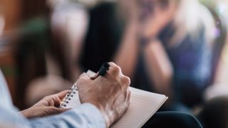 Woman writing on notebook in therapy session
