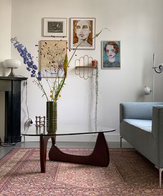 MCM lounge with sculptural glass and dark wood coffee table, and vase of tall flower stems, and gallery wall montage.