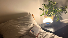 A dimly lit clean bedroom with a low bedside lamp and a book on the bed