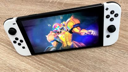 Nintendo Switch OLED on wooden surface, with Metroid Dread on the screen