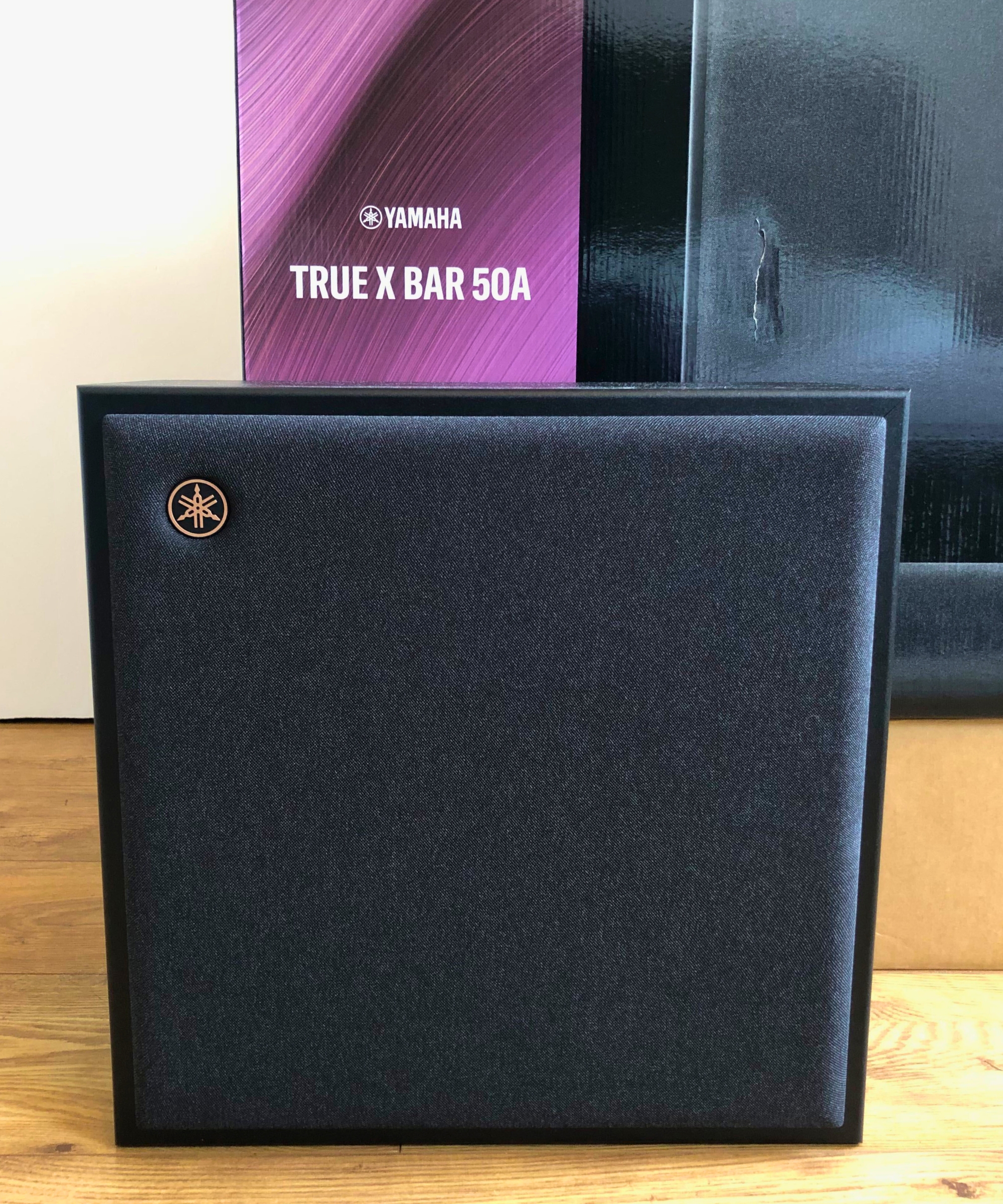 Yamaha True X Bar 50A subwoofer on wooden floor in Dan Fauzi&#039;s home in front of soundbar packaging.
