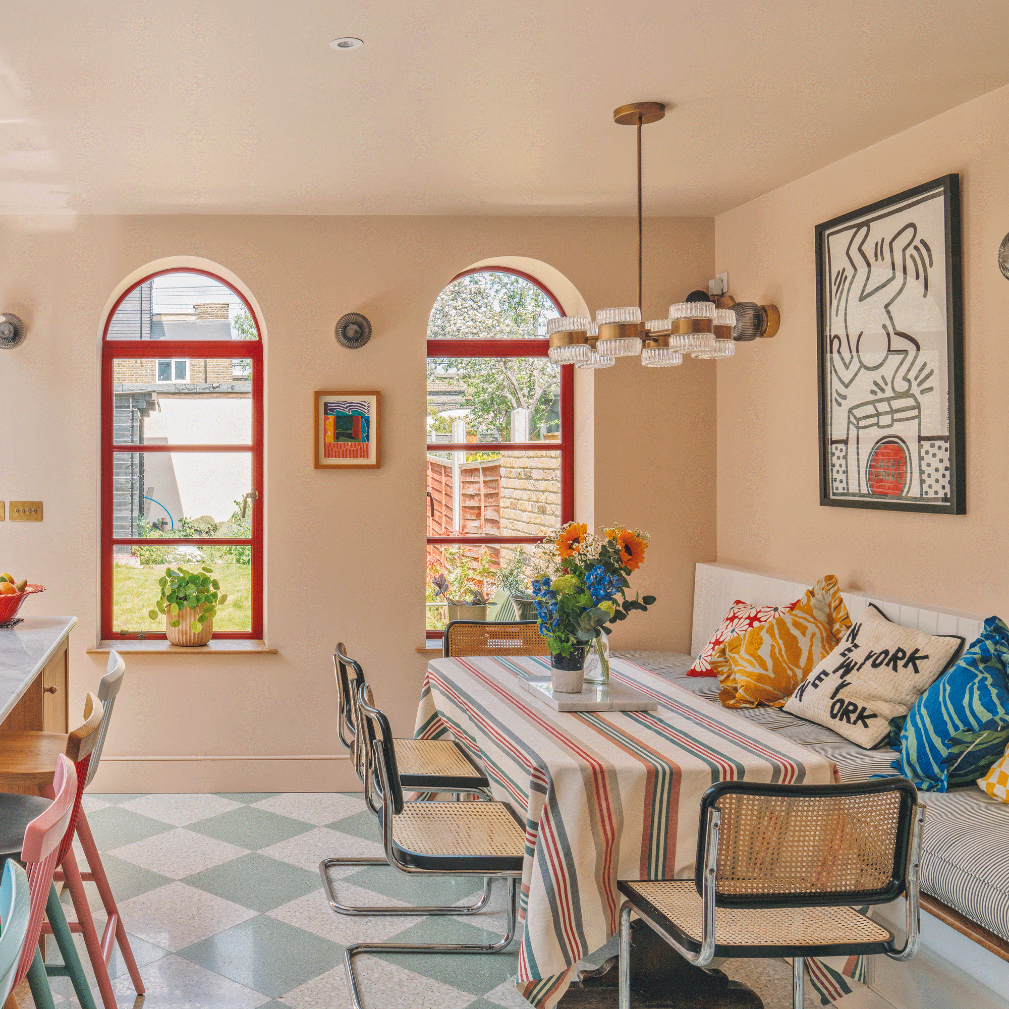 an open plan kitchen with a dining area with arched windows with red framed glazing a dining table with a striped tablecloth and striking wall art