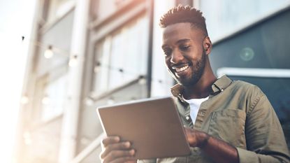 Young man smiling and using a tablet outside