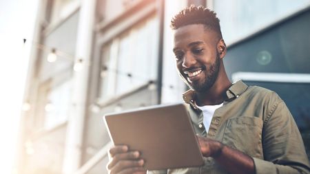 Young man smiling and using a tablet outside