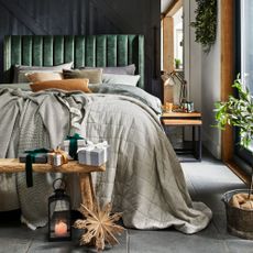 Cosy bedroom with green velvet headboard, pile of naturally coloured cushions and thick quilted throws