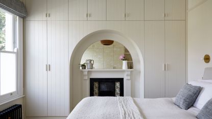 White bedroom with wall of built in storage over fireplace