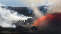 Volcanic eruption spouting glowing orange lava and thick smoke over rocky black terrain under a clear sky