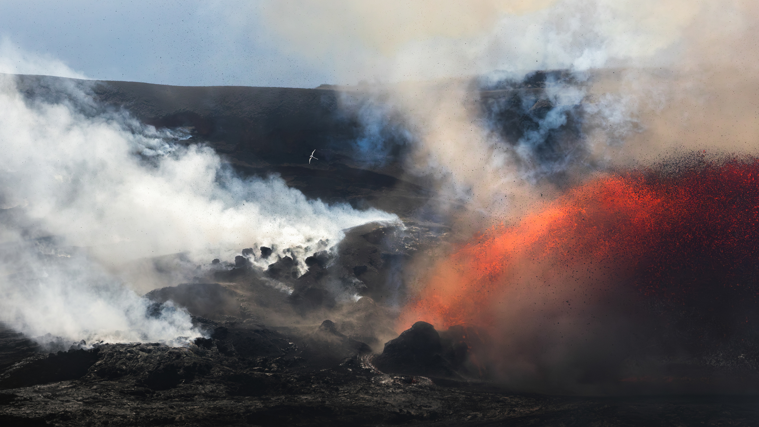 Volcanic eruption spouting glowing orange lava and thick smoke over rocky black terrain under a clear sky