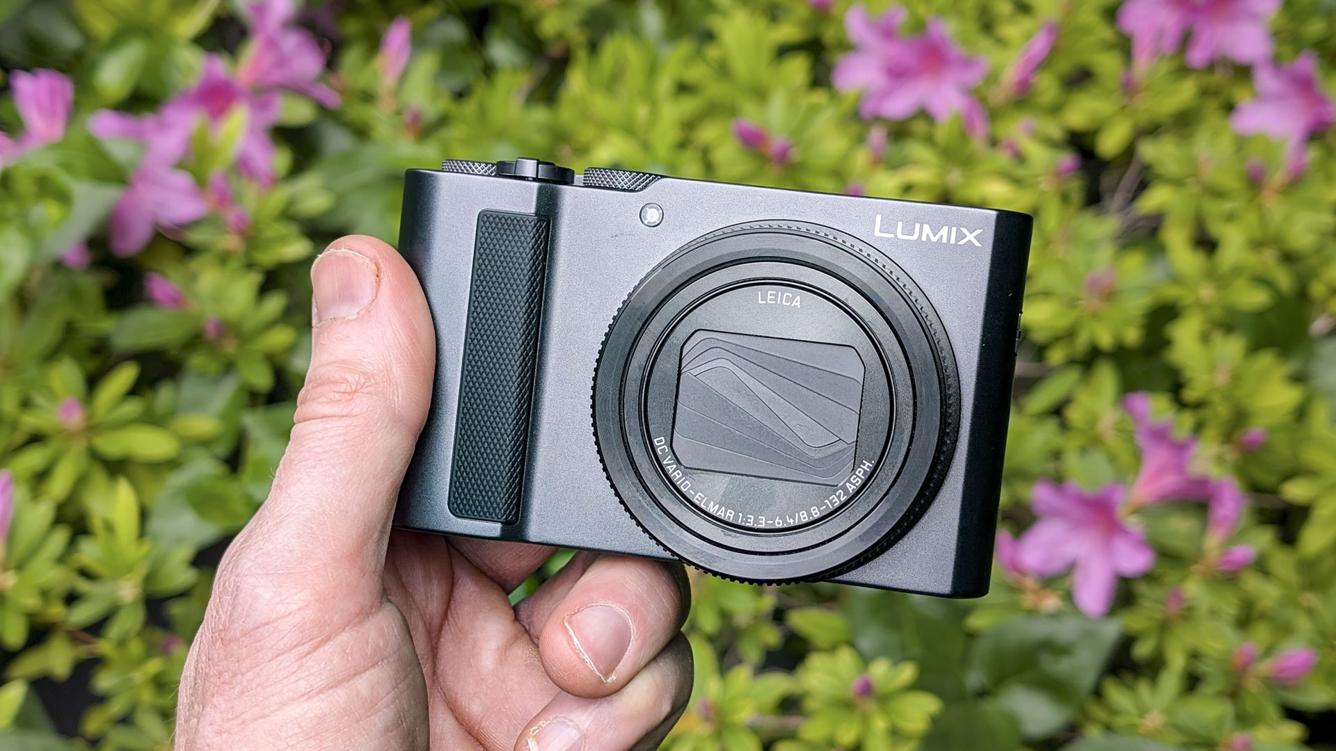Panasonic Lumix TZ300 compact camera in the hand with a colorful floral backdrop
