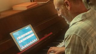 Man sits at a piano with the Simply Piano app open on his tablet