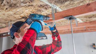 male worker lowering a ceiling using timber and cordless drill