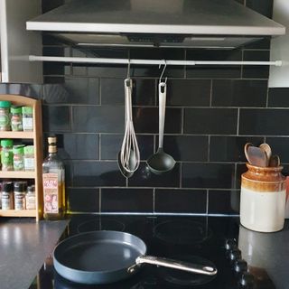 A kitchen hob with kitchen utensils hung above it on a tension rod