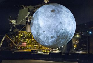 a full-size replica of a moon lander is partially blocked from view by a large globe of the moon