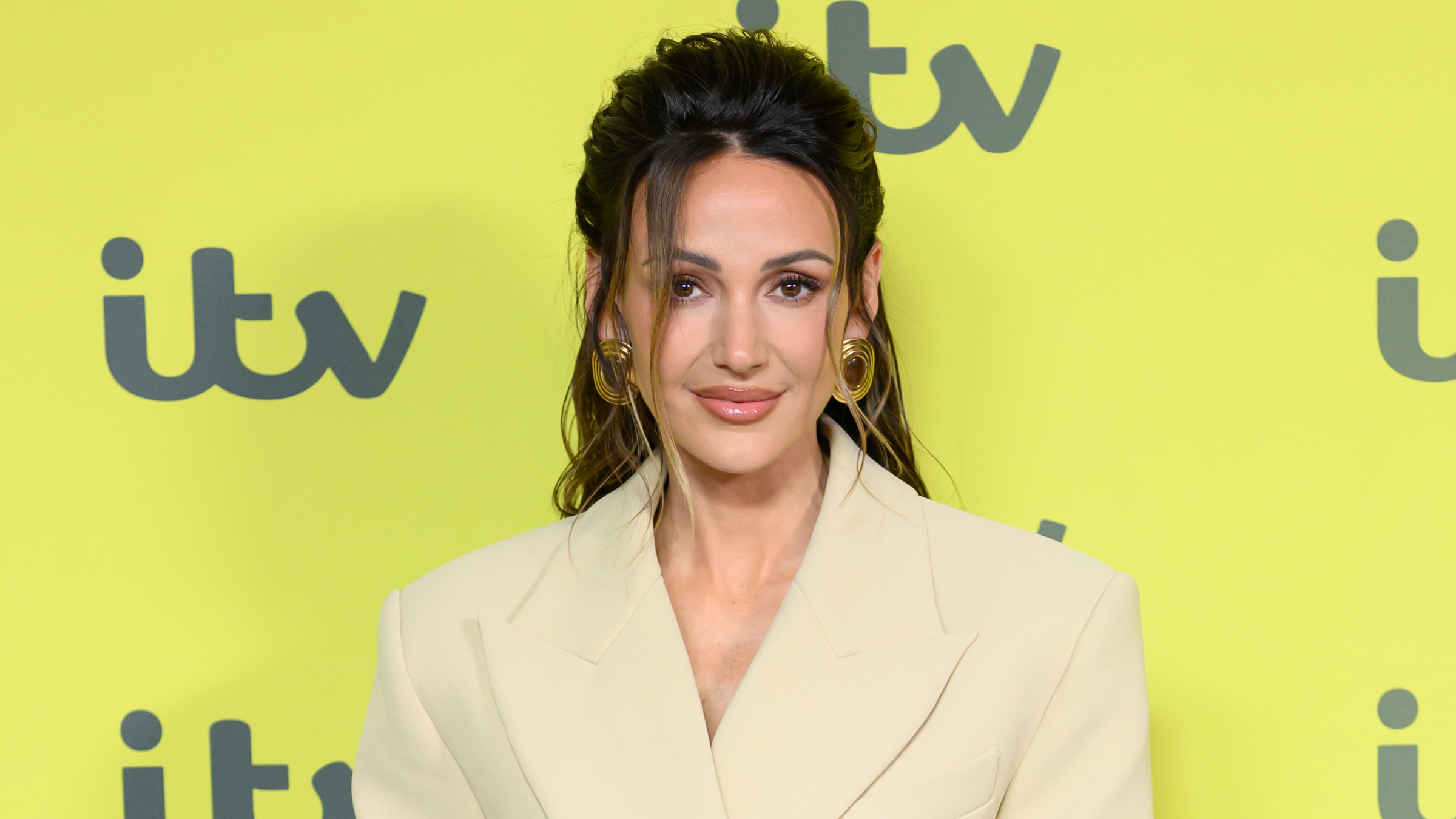 Michelle Keegan in beige suit in front of yellow ITV background.