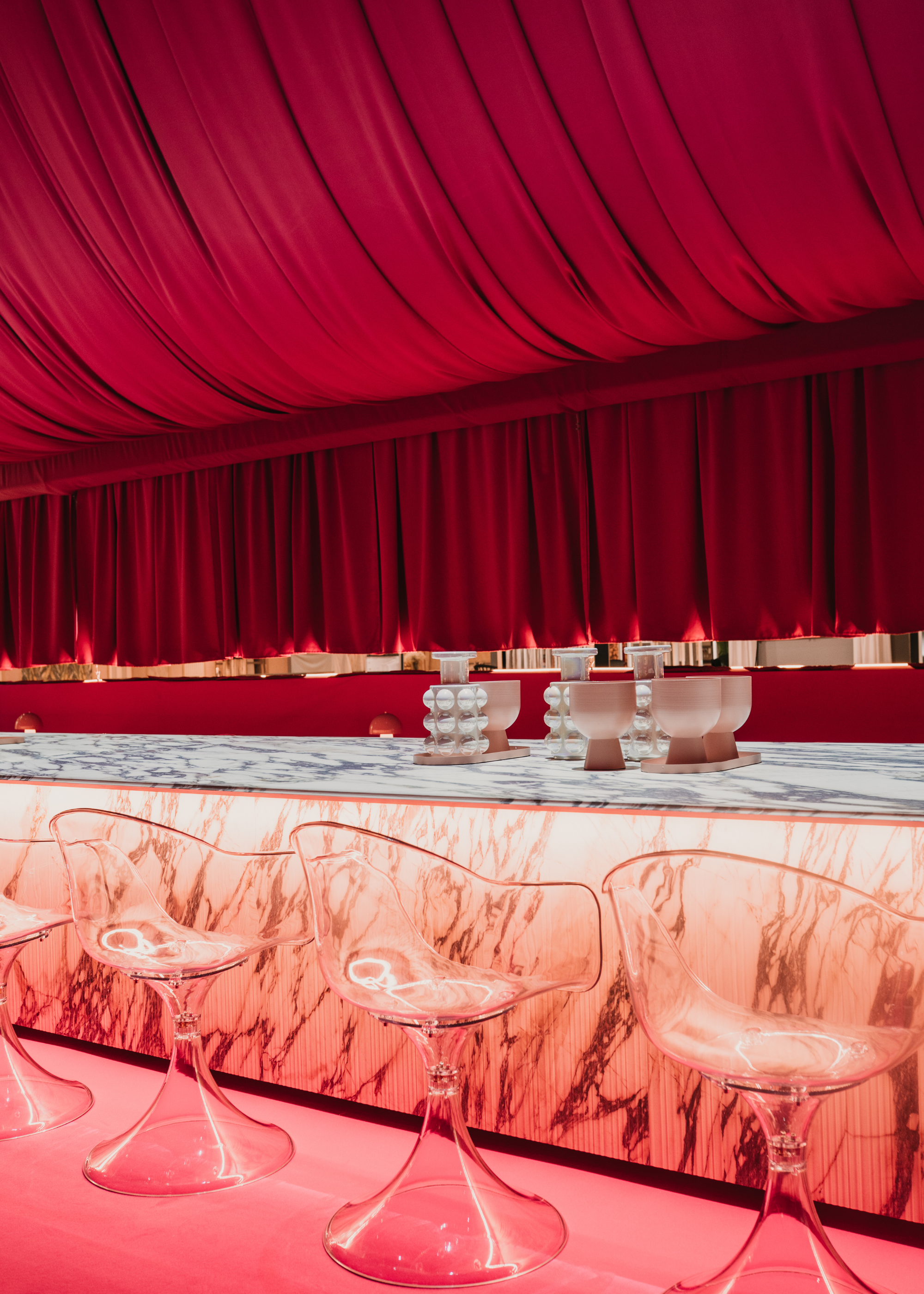A close-up of a room with pink curtain drapings and a 16-meter-long marble table featuring ceramic decor with a row of transparent stools along the side