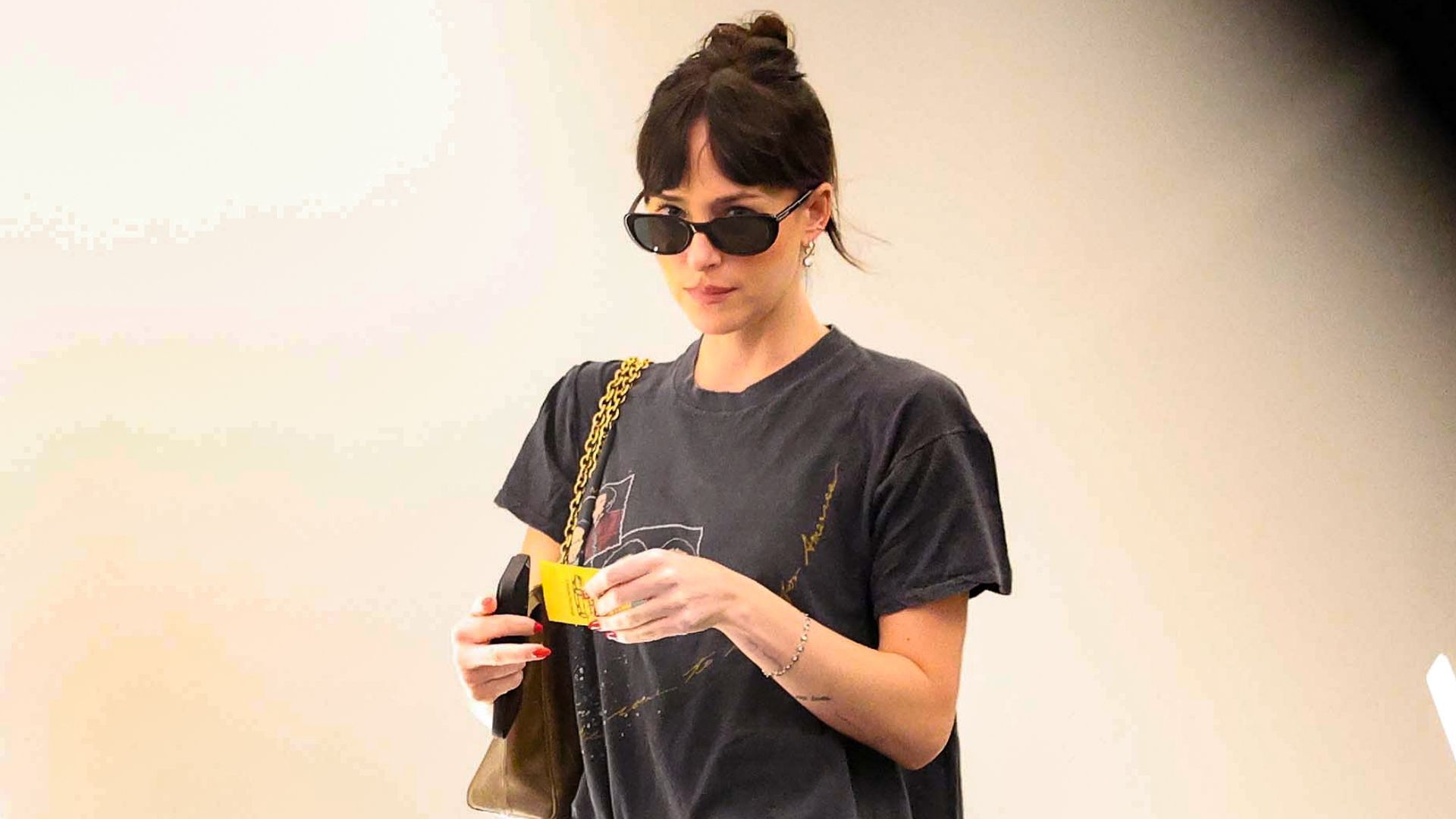 Dakota Johnson walks through an office building wearing brown baggy jeans with a black graphic t-shirt.
