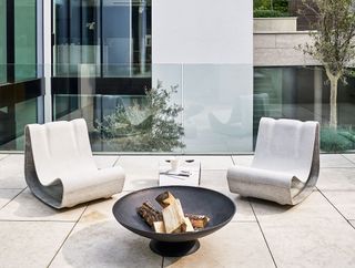 Modern outdoor patio furniture ideas featuring two sculptural metal chairs in front of a fire pit.