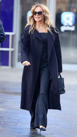 Amanda Holden wearing pinstripe jumpsuit, navy trench coat and navy accessories on February 05, 2025 in London