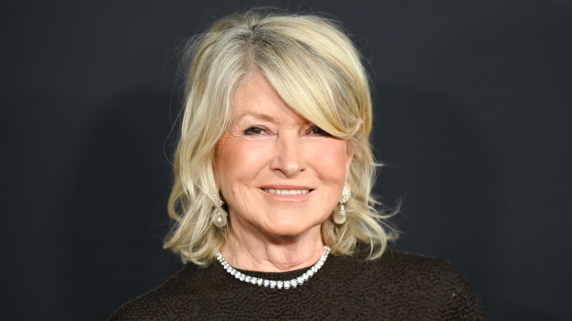a white woman with short, blonde hair poses for a photo in front of a black background