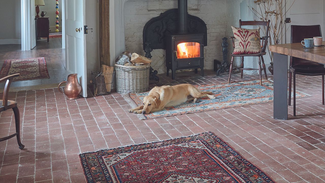 Living room with fire with dog in front and brick floor and chairs and dining table