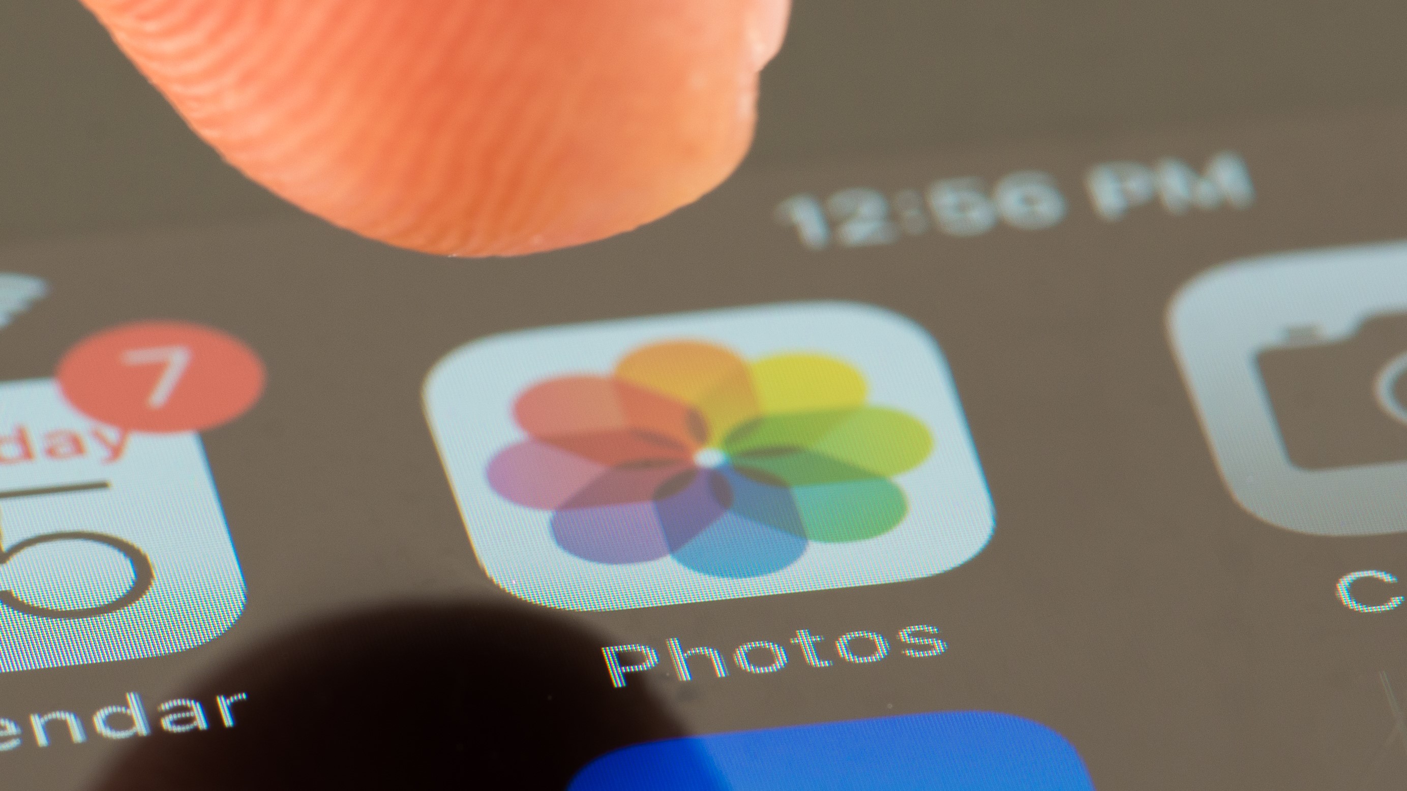 Un dedo se levanta para tocar el ícono de la aplicación Fotos en un iPhone
