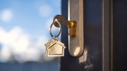 A close-up of a gold key and keychain shaped like a house. The key is in a home's lock. Conveys the ideas of renting, buying or selling a house, as well as mortgage rates.