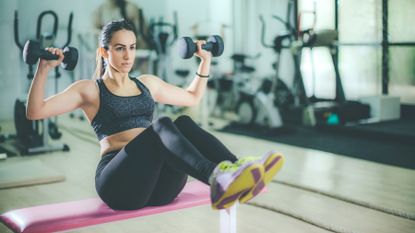 Woman lifting dumbbells while in a v-sit position