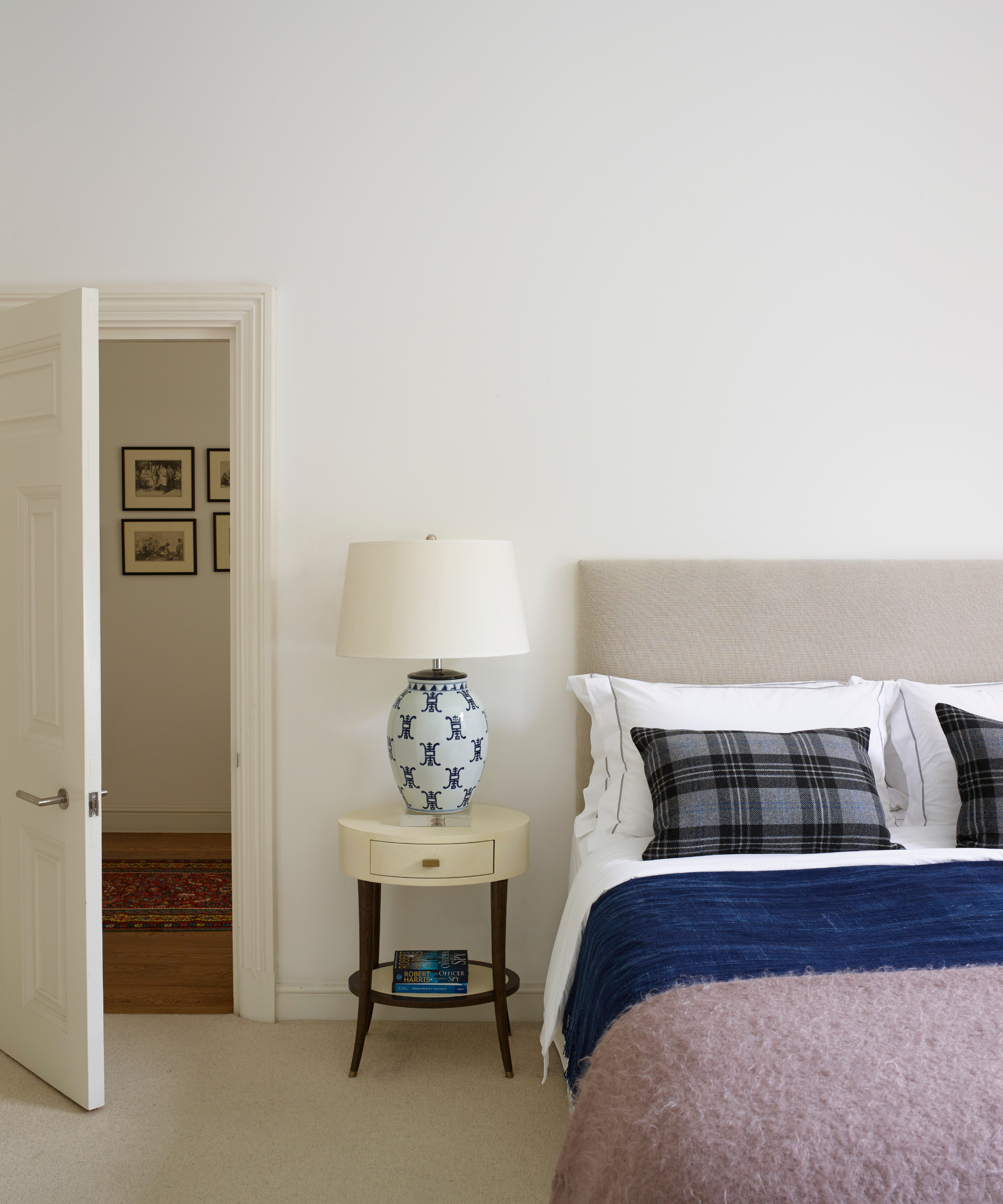 a bedroom with white walls, a small bedside table with a lamp, and a bed with blue and purple blankets on the bed