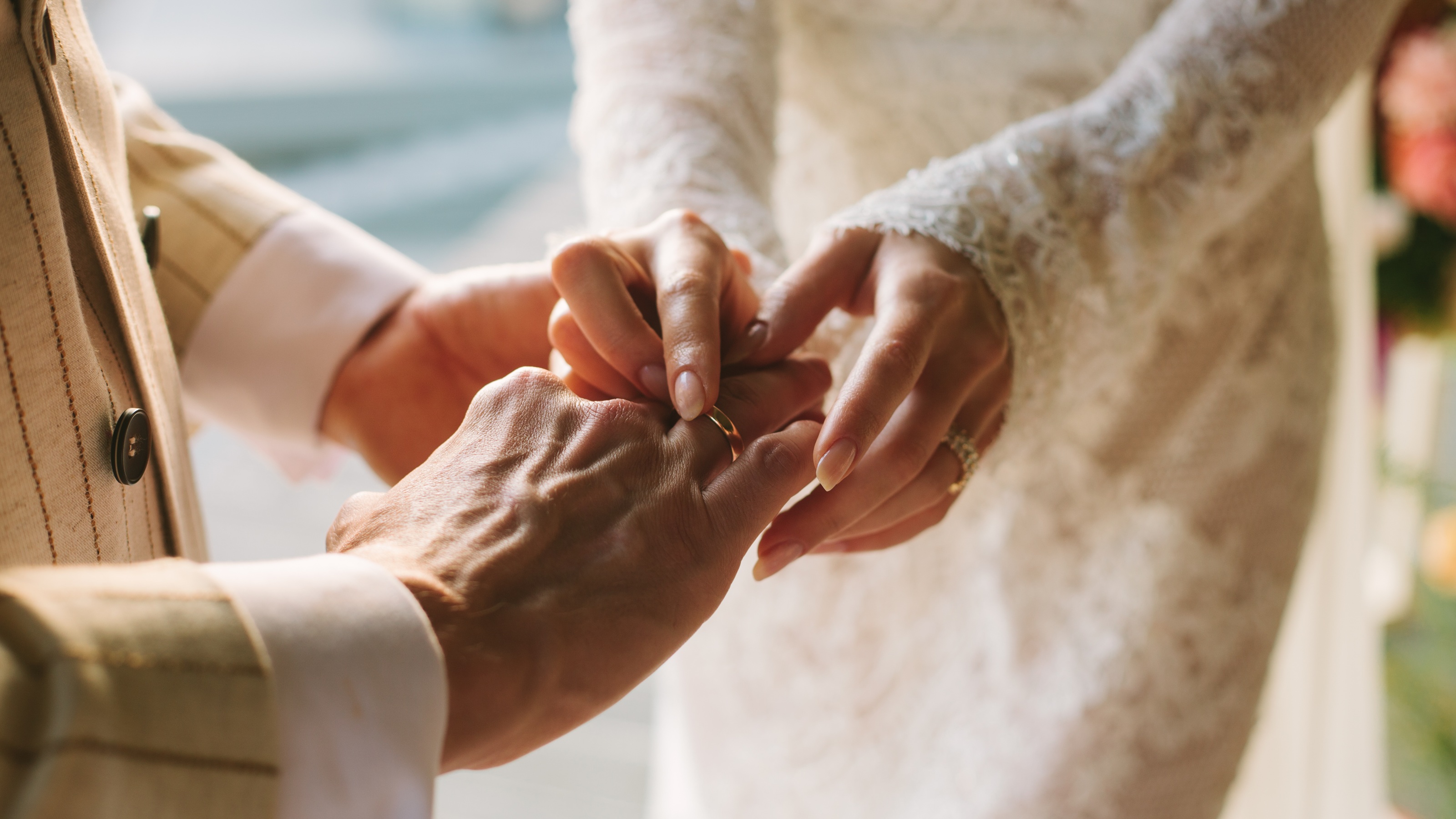 A bride slides a wedding ring onto her groom&#039;s hand.