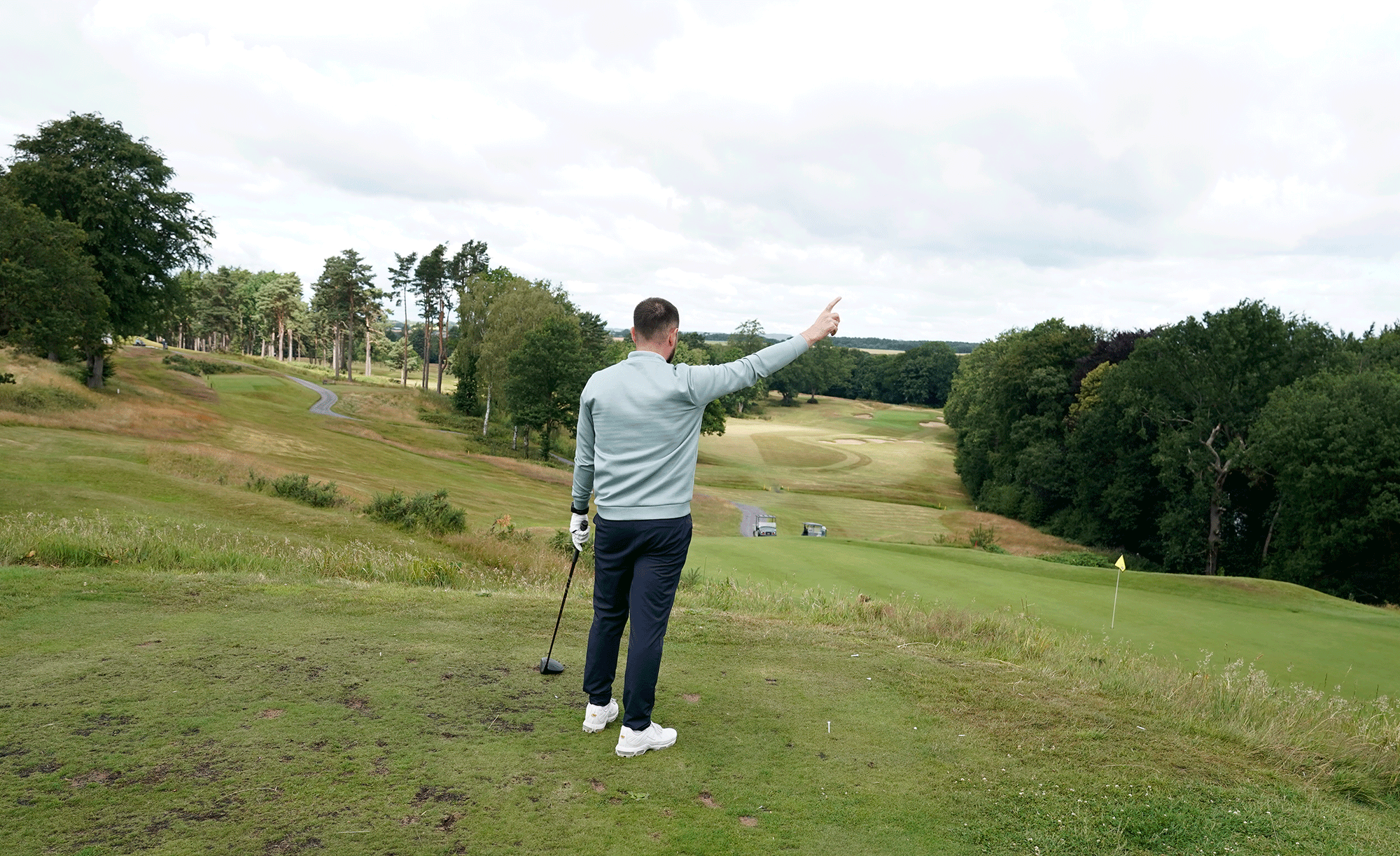 Baz Plummer pointing towards the hazard after hitting a wild slice off the tee