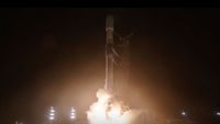 a black and white rocket launches into the night sky, the thrust from its engines casting light on the launch pad.