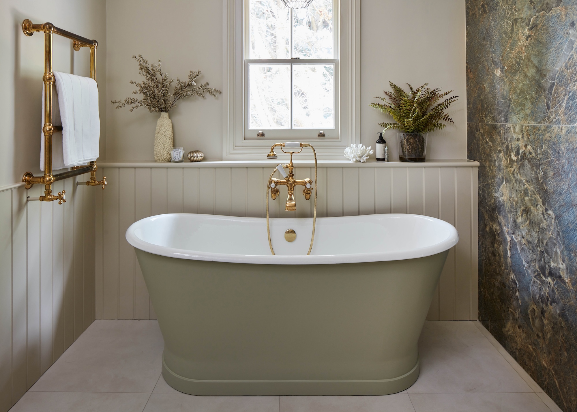 A freestanding bath painted in sage green shown with warm neutral walls and a feature wall in green tones